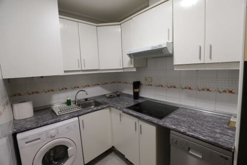 Cocina moderna con gabinetes blancos, encimeras de granito y electrodomésticos de acero inoxidable en propiedad de alquiler en Madrid