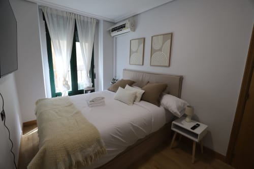 Elegante dormitorio en Madrid con cama queen, decoración neutra, cortinas verdes y mobiliario moderno en Innoval Rental Properties