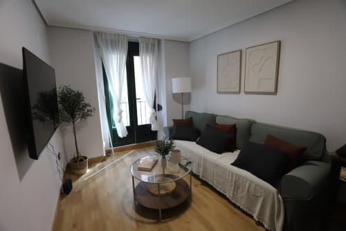 Sala de estar moderna en apartamento madrileño con sofá verde, televisor, mesa de café redonda y puertas a balcón con vistas a la ciudad en Innoval