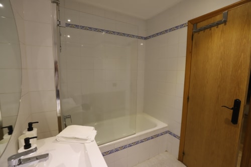 Baño moderno con azulejos blancos tipo metro, ducha de cristal, puerta de madera y cenefa decorativa azul en alquiler de Madrid
