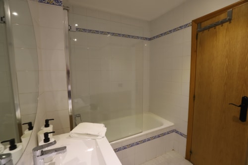 Baño moderno con azulejos blancos, cabina de ducha en cristal y puerta de madera en el Espacio Elegante de Innoval en Madrid