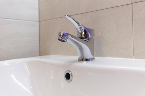 Rubinetto moderno in cromato e bianco presso l'Aurum Nolana Suites di Pompei, montato sopra lavabo in ceramica bianca con piastrelle beige