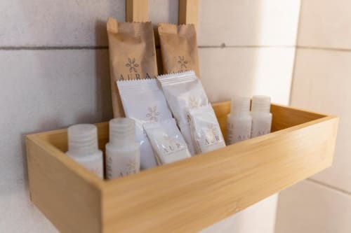 Scaffale in legno che espone i prodotti per l'igiene e il bagno Aurum in bottiglie bianche e sacchetti di carta kraft presso Aurum Nolana Suites,