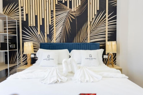 Lussuoso letto matrimoniale con biancheria bianca e cuscini brandizzati presso l'Aurum Nolana Suites a Pompei, con testata teal