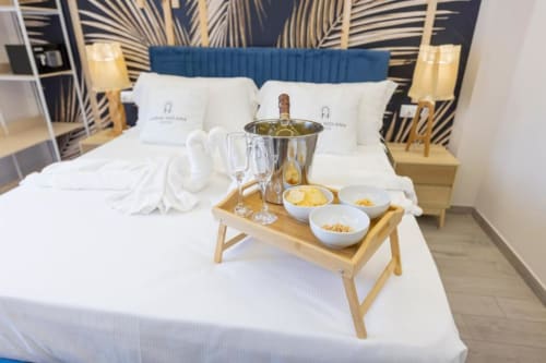 Deluxe Double Room presso Aurum Nolana Suites a Pompeii con bottiglia di vino, bicchieri e snack su vassoio in legno sul letto