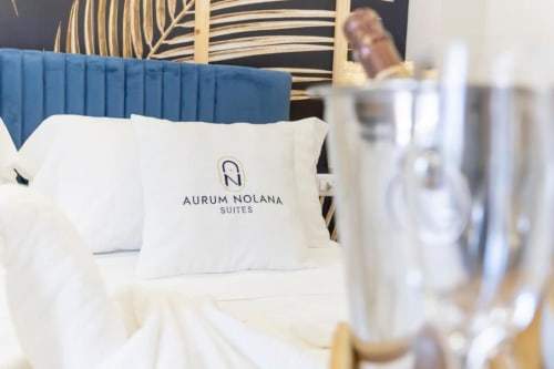 Camera deluxe Aurum Nolana Suites con letto, cuscino brandizzato, testata blu e vista sulla città di Pompei