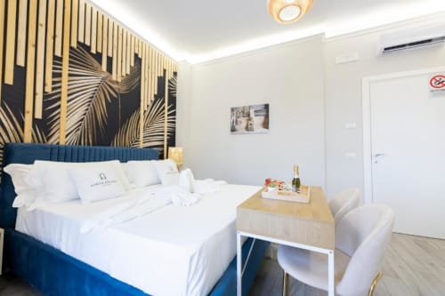 Camera doppia deluxe presso Aurum Nolana Suites a Pompei con letto imbottito blu, artwork con foglie dorate e vista moderna sulla città