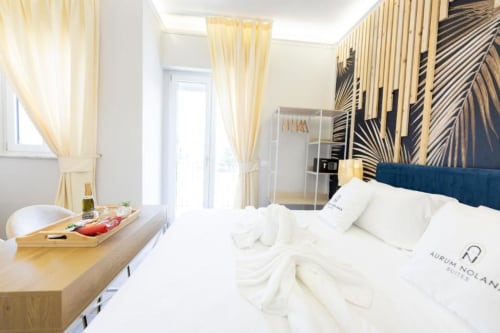 Camera doppia deluxe presso Aurum Nolana Suites a Pompei con testata blu, biancheria bianca, tendaggi crema e vista sulla città.