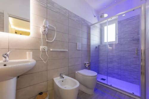 Bagno moderno in Aurum Nolana Suites Pompeii con doccia illuminata in blu, bidet, WC, lavabo e illuminazione ambientale