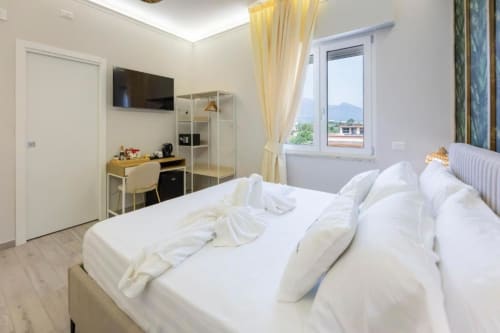 Luminosa camera tripla presso Aurum Nolana Suites a Pompei con vista sul Vesuvio, biancheria bianca, scrivania, TV e arredamento moderno