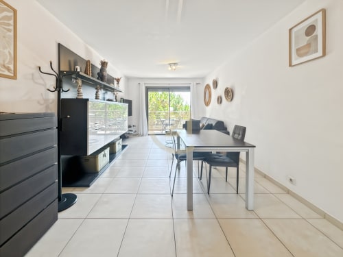 Séjour et salle à manger ouverts et modernes avec mobilier noir, carrelage et portes vitrées donnant sur la verdure