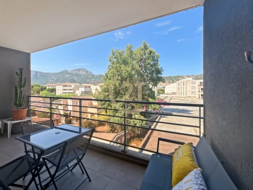 Terrasse ensoleillée de l'appartement L'Île-Rousse avec vue montagne, amandier et coin détente