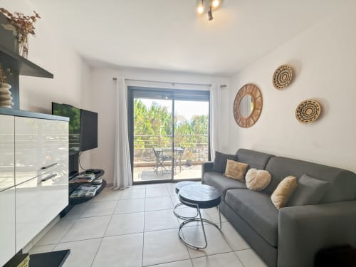 Salon moderne avec canapé gris, téléviseur et baies vitrées donnant sur balcon avec vue sur L'Île-Rousse, Corse