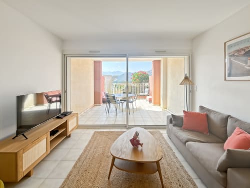 Séjour moderne à L'Île-Rousse avec canapé gris, mobilier bois et terrasse ouverte sur vue montagne