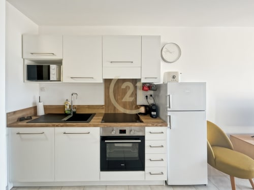 Cuisine moderne blanche avec plan de travail en bois, cuisinière noire, réfrigérateur inox et micro-ondes à Calvi T2
