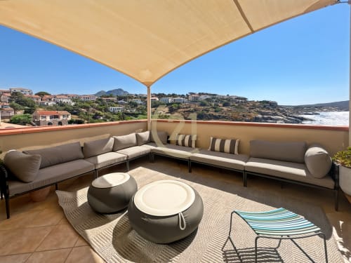 Parasol beige ombrageant une terrasse spacieuse avec transats offrant une vue panoramique sur la côte de L'Île-Rousse et la Méditerranée