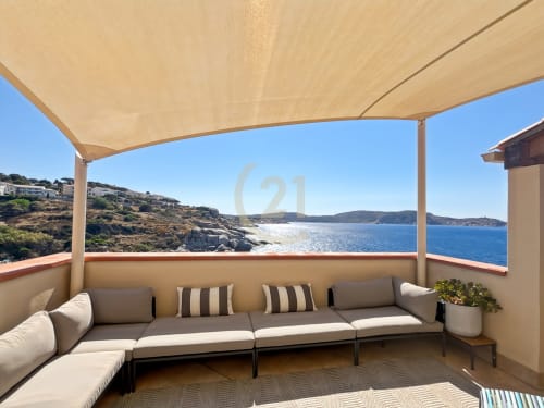 Terrasse beige ombragée avec sièges gris dominant la mer bleue et la côte rocheuse de l'appartement L'Île-Rousse