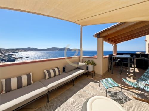 Terrasse côtière à L'Île-Rousse avec salon, coussins rayés, vue mer et eaux méditerranéennes bleues au-delà des rochers