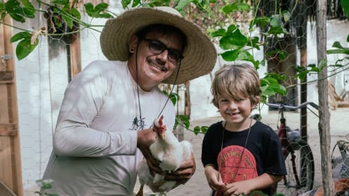 Homem e criança segurando uma galinha na La Cozinha Pousada e Restaurante em Cajueiro da Praia, Brasil