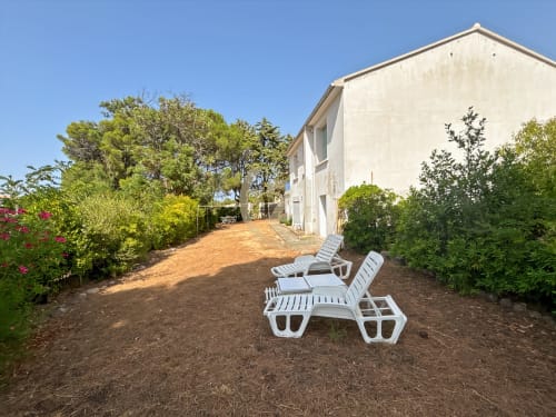 Chaises longues blanches sur la terrasse-jardin sablée de l'appartement Calvi à L'Île-Rousse, entourées de végétation méditerranéenne
