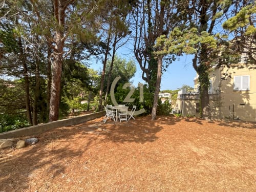 Terrasse de jardin ombragée avec mobilier de salle à manger sous de grands arbres, appartement à Calvi avec coin détente extérieur