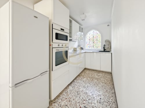 Cuisine moderne blanche avec électroménagers en acier inoxydable, carrelage en pierre et fenêtre cintrée dans un appartement à Calvi