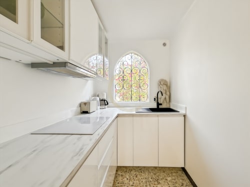 Cuisine moderne blanche avec comptoirs en marbre, fenêtre vitrail bombée donnant sur le jardin dans l'appartement de Calvi