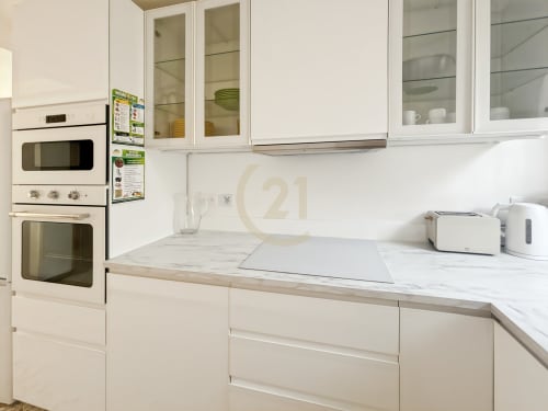Cuisine moderne blanche dans un appartement à Calvi avec fours intégrés, plan de travail en marbre et placards vitrés