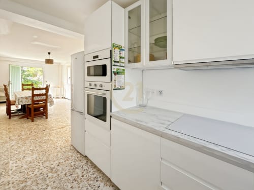 Cuisine blanche moderne avec double four, plan de travail en marbre et armoires vitrées, vue sur jardin de l'appartement à Calvi
