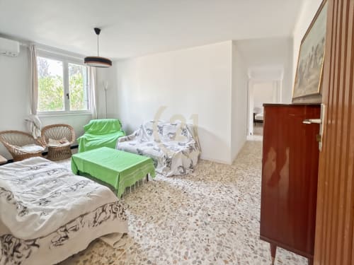 Spacieuse salle de séjour avec plusieurs lits, chaises en rotin, sol en terrazzo beige et vue sur le jardin d'une maison authentique à Calvi