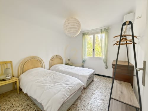 Chambre lumineuse avec deux lits simples, têtes de lit en rotin, luminaire suspendu et vue sur le jardin à L'Île-Rousse