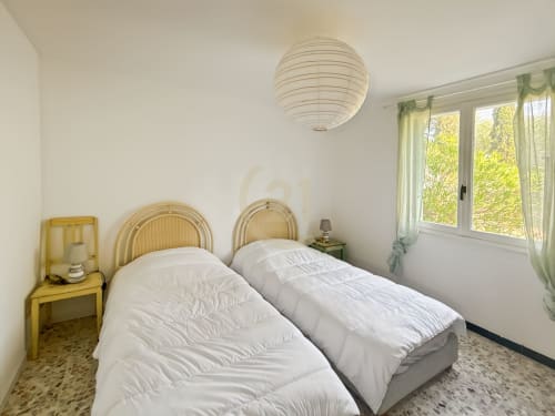 Chambre lumineuse avec deux lits simples, têtes de lit en rotin et vue sur jardin, propriété Century 21 à Calvi, Corse