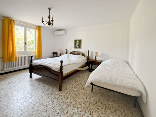 Chambre spacieuse avec deux lits, mobilier en bois foncé et rideaux jaunes donnant sur le jardin de l'appartement à Calvi