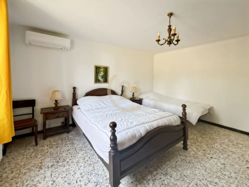 Chambre spacieuse avec lit en bois, draps blancs et mobilier classique à l'appartement Century 21 de Calvi, Corse