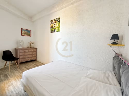Chambre lumineuse dans l'appartement de l'Île-Rousse avec lit blanc, commode en bois et chaise noire