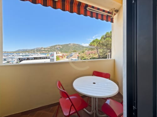 Terrasse avec table blanche et chaises rouges surplombant la marina et la plage de L'Île-Rousse