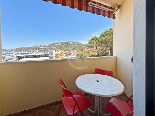 Terrasse avec table ronde blanche et chaises rouges surplombant la marina de L'Île-Rousse et les montagnes de Corse