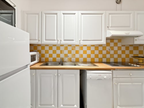 Petite cuisine avec armoires blanches, dosseret à carreaux jaunes et blancs, plan de travail en bois et évier en acier inoxydable