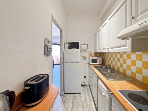 Cuisine galley moderne avec dosseret en carrelage jaune-blanc, comptoirs en bois, appareils blancs et porte avec vue sur mer