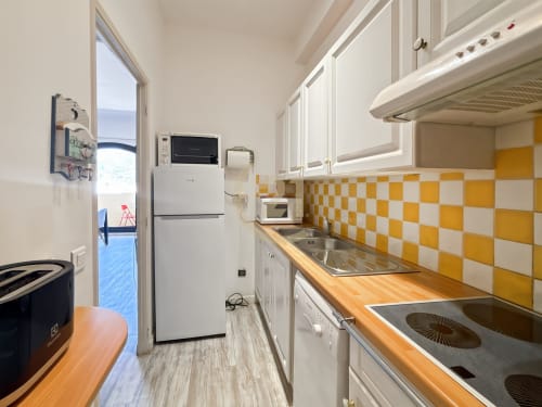 Cuisine moderne avec carrelage à damier jaune, comptoirs en bois et vue sur la mer depuis l'appartement de L'Île-Rousse