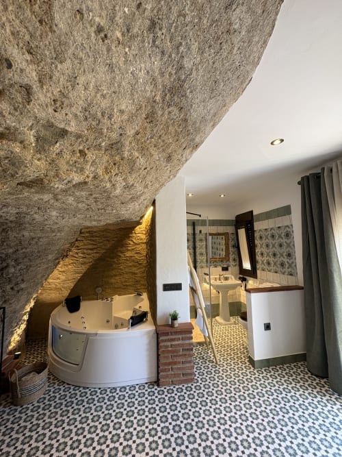 Baño de apartamento cueva de lujo con muros de piedra, bañera de hidromasaje, iluminación ambiental y azulejos con patrones en La Joya de Setenil