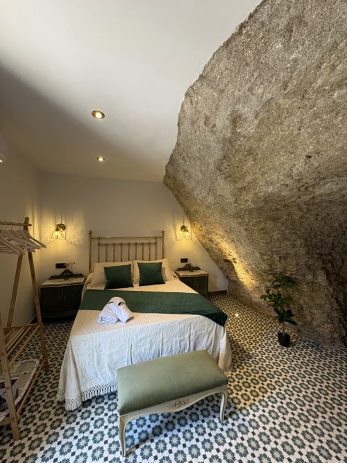 Lujosa habitación en cueva de La Joya de Setenil con paredes de piedra, ropa de cama verde e iluminación cálida en Setenil de las Bodegas.