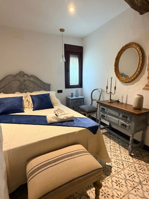 Dormitorio elegantemente amueblado en La Joya de Setenil con acentos azules, espejo ornamentado y decoración tradicional de casa cueva andaluza