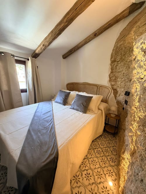 Dormitorio rústico en cueva de La Joya de Setenil con muros de piedra vista, vigas de madera e iluminación cálida