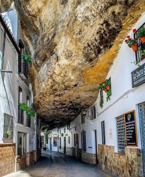 Calle cueva de Setenil de las Bodegas con casas de muros blancos bajo un dramático saliente rocoso, La Joya de