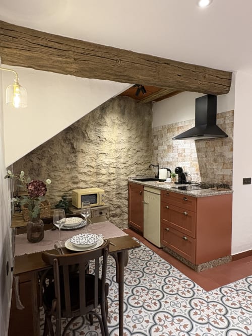 Cocina de apartamento cueva con vigas de madera rústica, muros de piedra, mesa de comedor y azulejos españoles tradicionales en La Joya