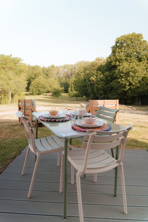 Espace de restauration extérieur au Hameau de Céline avec table et chaises modernes sur terrasse en bois dominant des champs verdoyants et des arbres