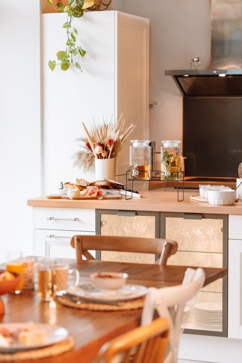 Salle à manger du Hameau de Céline avec table dressée, composition de fleurs séchées, distributeurs de boissons et comptoir de cuisine moderne