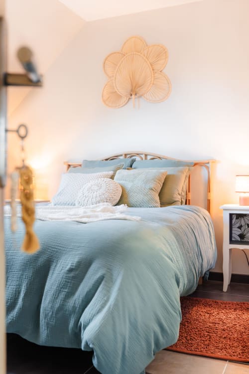 Chambre douillette au Hameau de Céline avec parure bleue, coussins décor, art floral en bois et éclairage ambiant chaleureux