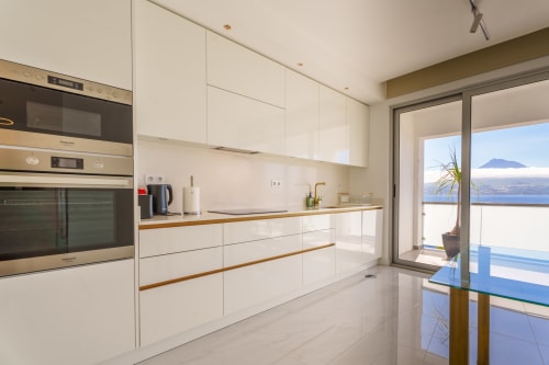 Modern white kitchen with wood countertops, stainless steel appliances, and ocean view of Faial island at Suites Avenue Lux